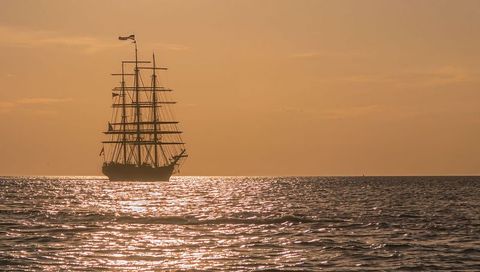 Tall ship sailing on calm sea during golden sunset