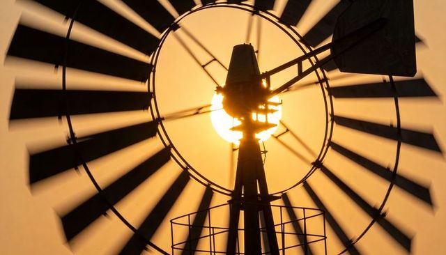 Backlit multi-blade windmill silhouette framing sun with radial spokes and tower