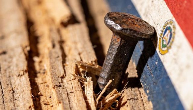 Rusting forged nail driven into splintered wood plank with painted stripe emblem macro