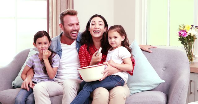 Family seated on sofa in living room, eating popcorn together. Perfect for illustrating family time, domestic bliss, togetherness, casual lifestyle, and home comfort.