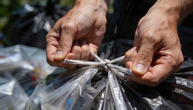 Tying black bin bag knot with hands closeup, twisting clear liner, outdoor cleanup