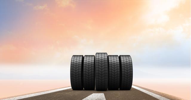 Row of car tires placed on road stretching towards horizon with colorful sky. Ideal for automotive advertisements, road safety campaigns, vehicle maintenance promotions, tire manufacturing industry use.