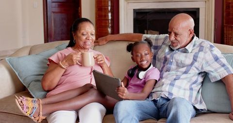 Happy grandparents and granddaughter bonding over a tablet on sofa