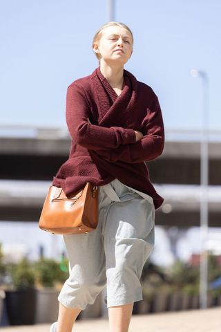 Confident woman walking in maroon knit sweater carrying tan leather bag on urban sidewalk