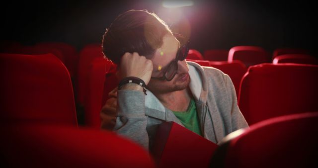 A young Caucasian man appears stressed or disappointed while sitting alone in a movie theater, with copy space. His body language suggests he might be reacting to an intense or unsatisfactory moment in the film.