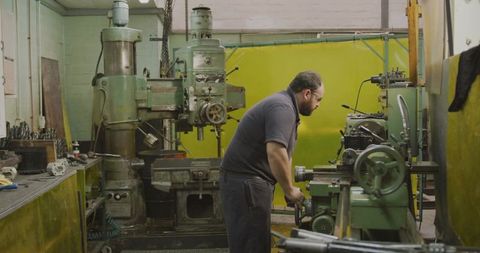 Skilled machinist working at lathe in industrial workshop