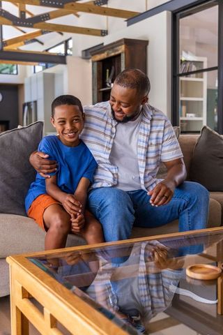 African american father and teen son sharing warm moment on sofa in modern cozy home