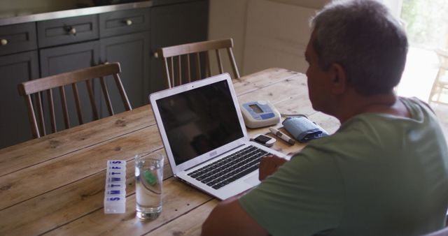 Senior Man at Home Using Laptop with Medication and Healthcare Devices - Download Free Stock Images Pikwizard.com