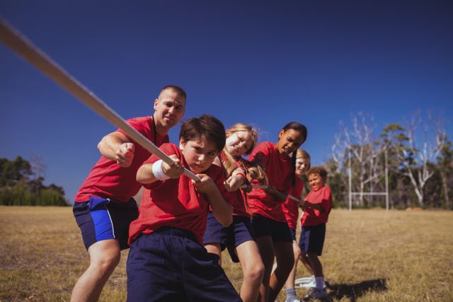 Trainer assisting kids in tug of war during obstacle course training in boot camp. Ideal for use in articles about teamwork, outdoor activities, children's sports, and fitness training programs.