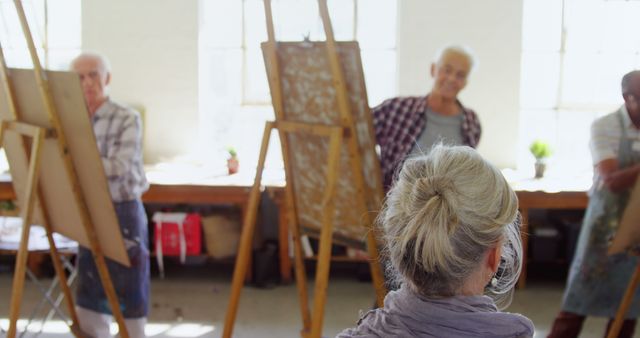 Senior citizens are actively participating in a painting class, each one is working on an easel in a well-lit art studio. This image might be used to highlight lifelong learning activities, senior hobbies, art therapy, creative workshops for elderly people, or promoting wellness programs for retirees.