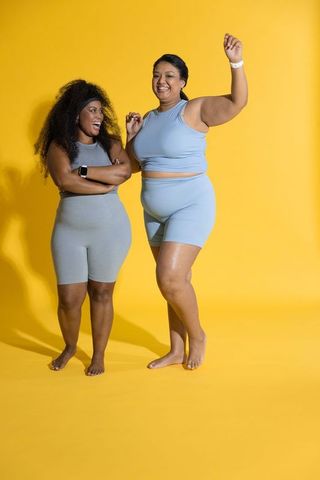 Joyful diverse women posing and laughing in matching activewear on yellow backdrop