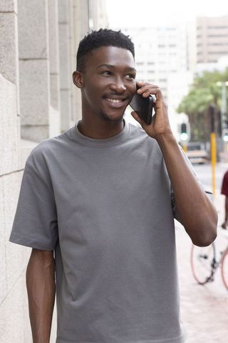 African american man smiling and talking on smartphone on urban sidewalk casual portrait