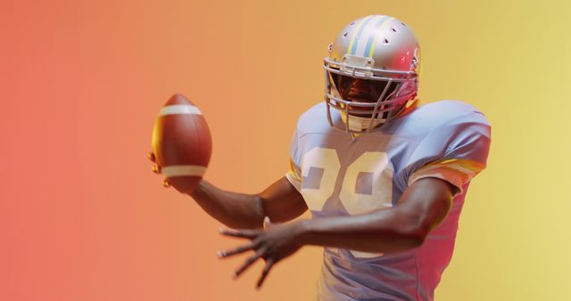 Image of african american american football player with ball over yellow to orange background. American football, sports and competition concept.