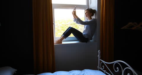Woman Sitting on Window Sill Taking Selfie at Home