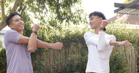 Male friends stretching outdoors with fitness smartwatches in backyard