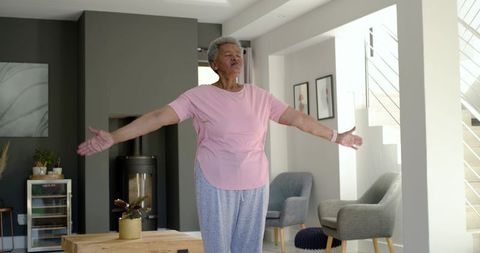 Senior african woman stretching arms in sunlit modern living room practicing morning stretch