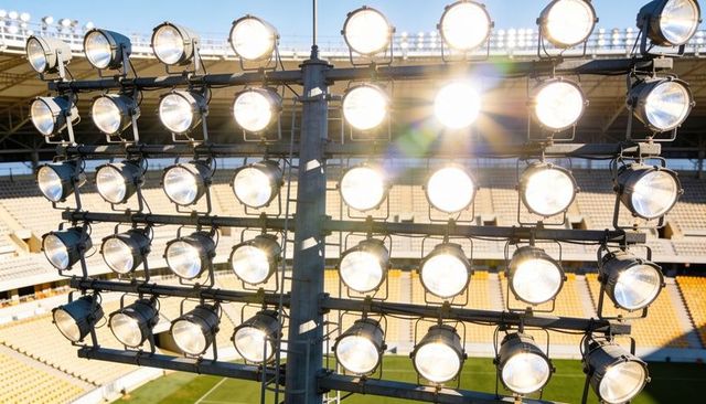 Floodlights illuminating stadium pitch with strong lens flare and steel rigging