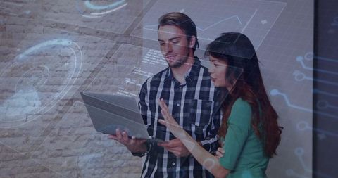 Young professionals collaborating over laptop with holographic data overlay and dashboard