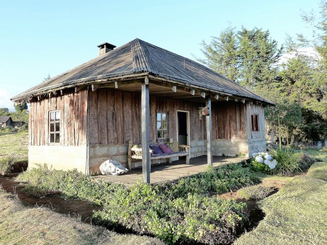 Rustic wooden cabin located in rural countryside, surrounded by greenery and simple natural beauty. Ideal for use in articles and advertisements related to travel destinations, rural living, sustainable lifestyle, tranquil retreats, and traditional home designs.