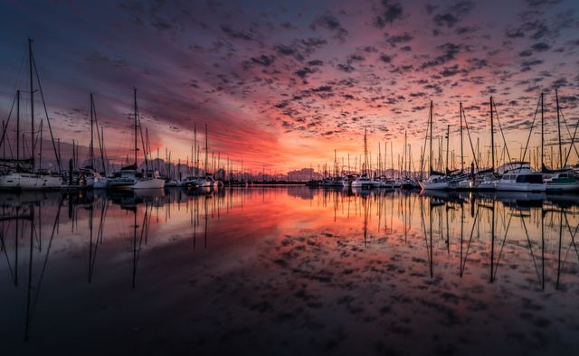 Vibrant sunset reflecting in calm marina waters with docked boats and yachts. Ideal for travel websites, nature blogs, and inspiration for peaceful settings.