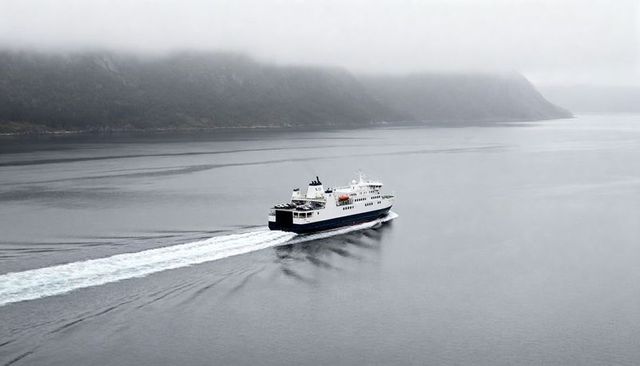 Ferry sailing through foggy fjord leaving wake and lifeboats for maritime transport