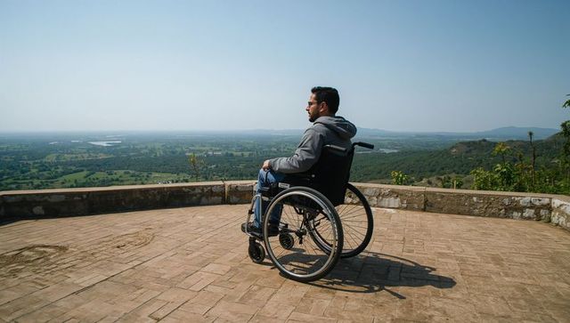 Man in wheelchair gazing over rolling farmland from hilltop terrace, independence