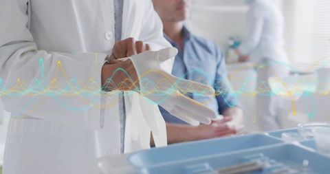Doctor putting on gloves beside exam tray with patient waiting for clinical examination