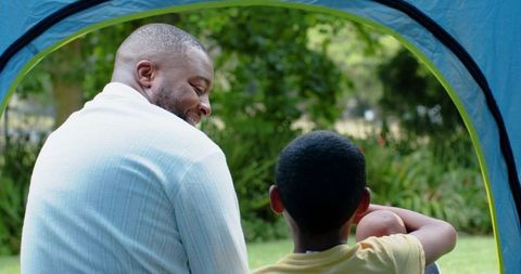 African american father and son bonding in backyard tent relaxing on lawn