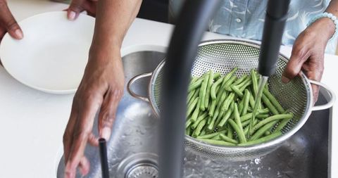 Senior women washing fresh green beans in kitchen sink