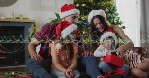 Family celebrating christmas morning opening gifts under tree wearing santa hats
