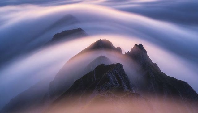 Jagged alpine ridge rising through ribbon clouds at sunrise with mist-wrapped spires