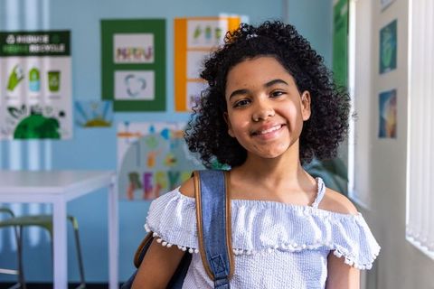 African american preteen girl smiling with denim backpack in colorful classroom sunlight