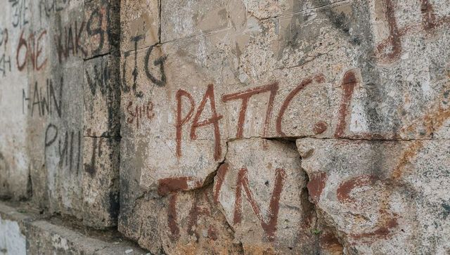 Weathered limestone wall with red-brown graffiti, flaking mortar and cracked texture