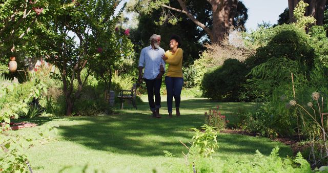 Happy african american couple holding hands and walking in sunny garden. staying at home in isolation during quarantine lockdown.