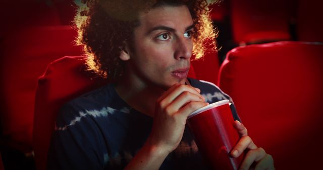 Young Man with Curly Hair Enthralled while Drinking Soda in Movie Theater - Download Free Stock Images Pikwizard.com