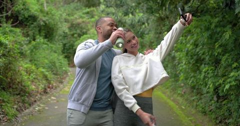Couple on forest trail taking selfie after outdoor workout drinking water in activewear