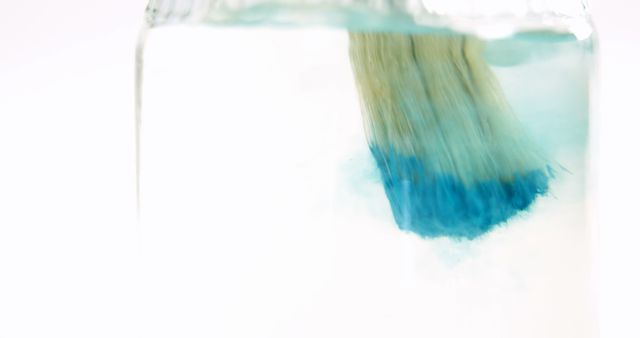 Close-up of paintbrush with blue paint being washed in water against white background