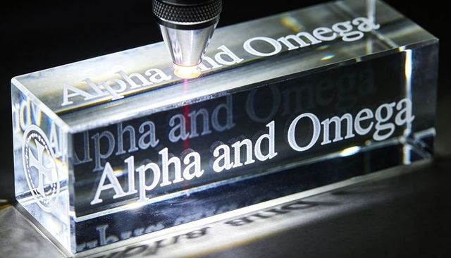 Laser engraving clear acrylic block with alpha and omega etching on reflective benchtop