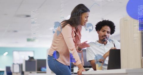 Colleagues collaborating over laptop with augmented data overlays in open-plan office