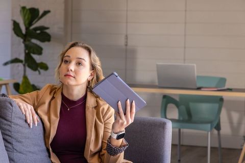 Thoughtful professional woman holding tablet folio on sofa in contemporary coworking lounge