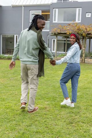 African american couple walking hand in hand on lawn outside modern gray home