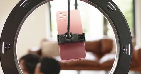 Ring light smartphone setup with pink phone recording diverse couple on brown leather sofa