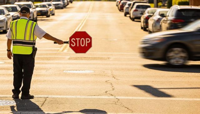 Crossing guard holding stop sign directing traffic at sunlit urban intersection golden hour