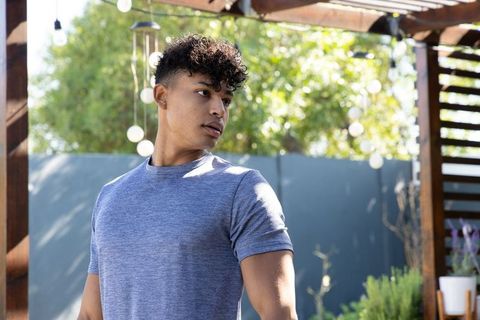 Young man standing under pergola on patio wearing heather-gray tee looking left