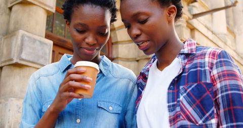 African American Twin Sisters Smiling and Using Phone Outdoors