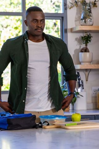 African american man packing healthy lunch at kitchen counter wearing dark green shirt