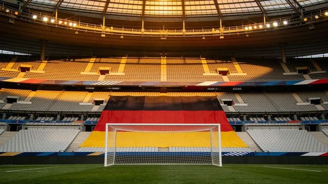 Sunlit german flag draping stadium stands behind white soccer goal on empty pitch