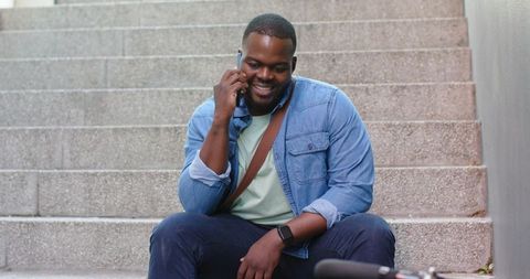 Smiling African American man talking on smartphone while sitting on urban steps