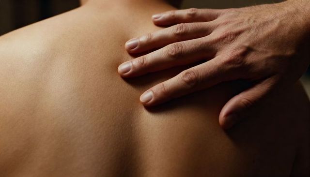 Hand resting on bare upper back conveying intimacy and tenderness, close-up skin texture