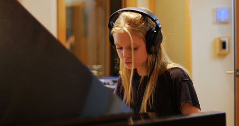 Young Woman Wearing Headphones Playing Piano in Music Studio